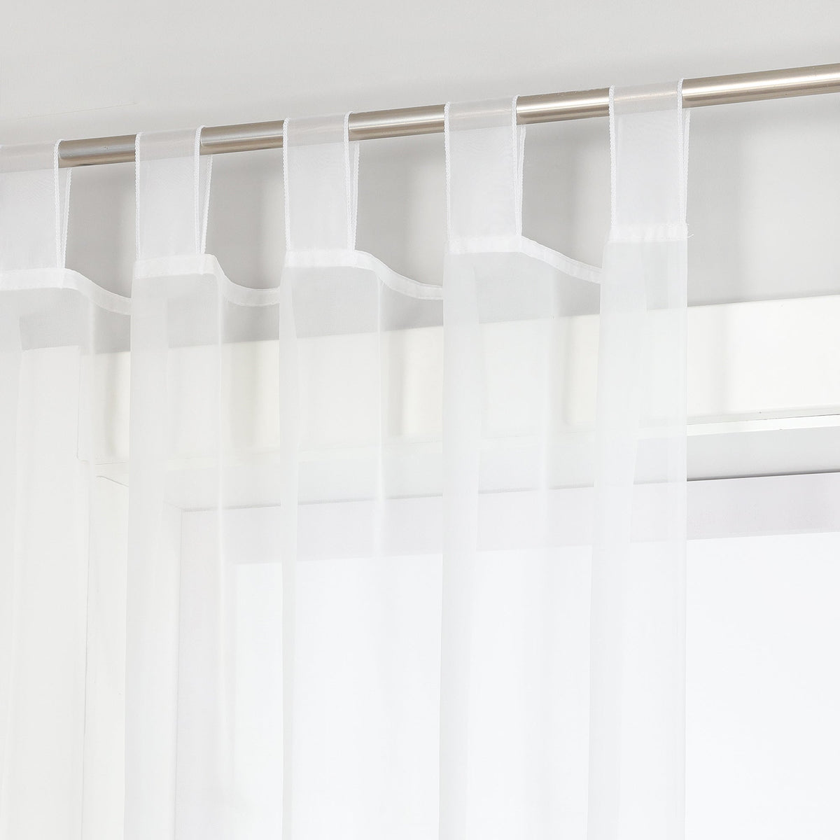 Das Bild zeigt eine Vorhangstange, an der weiße Voile-Vorhänge hängen. Die Vorhänge sind mit Haken an der Stange befestigt, und durch die Voile-Vorhänge ist ein Teil des Fensters sichtbar. Insgesamt vermittelt das Bild einen einfachen und hellen Eindruck.