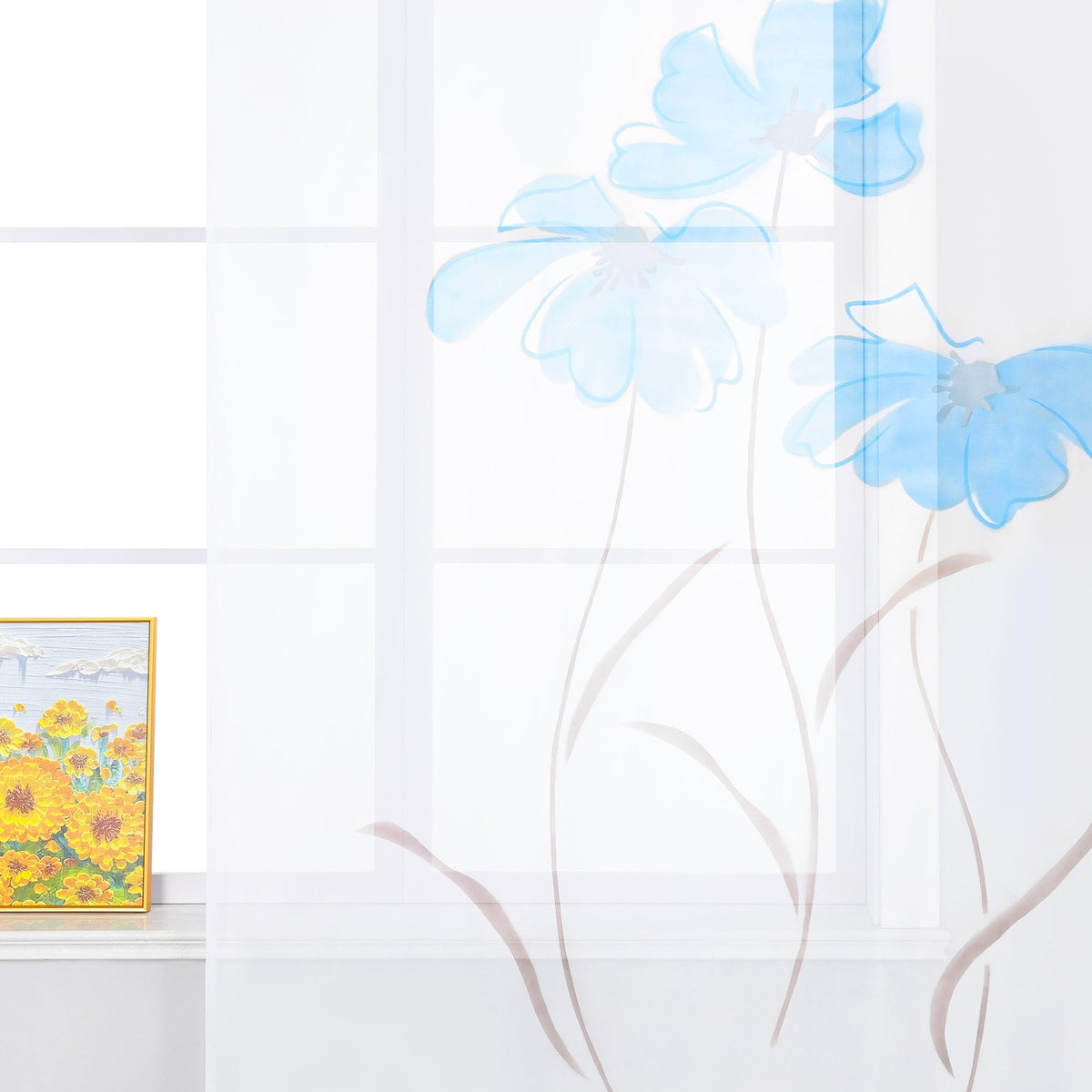 Das Bild zeigt einen weißen Vorhang mit blauen Blumenmustern. Das Design lässt die Blumen wie in der Luft schwebend erscheinen. Auf der Fensterbank steht ein dekoratives Bild, das gelbe Blumen darstellt. Insgesamt vermittelt die Szene einen frischen und hellen Eindruck.