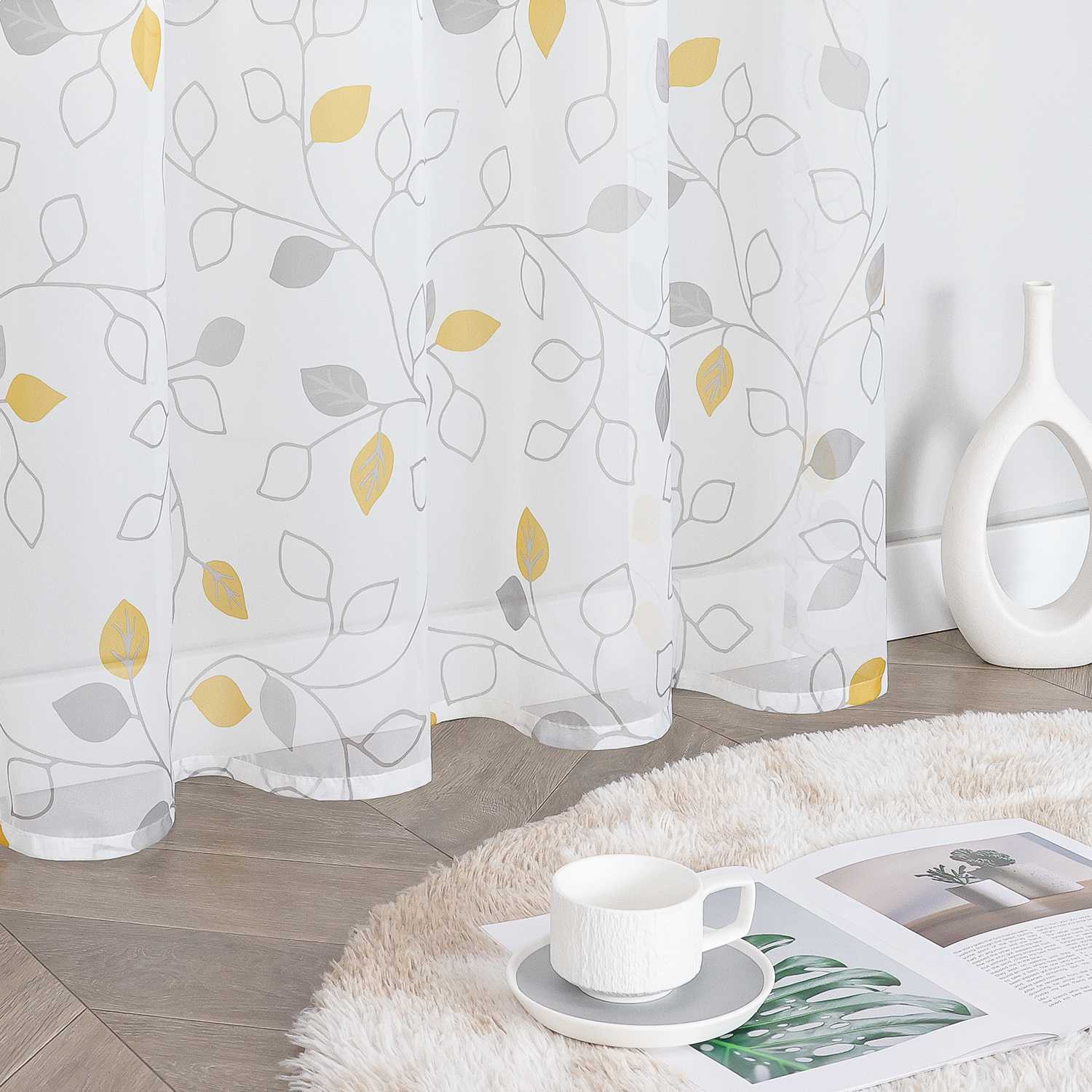 Dieser weiße Voile-Vorhang mit grauen Zweigen und gelb-grauen Blättern ist leicht und durchscheinend. Neben dem Vorhang steht eine weiße Vase, auf dem flauschigen Teppich liegen eine Tasse mit Untertasse und ein Magazin. Der Vorhang eignet sich perfekt für die Heimdekoration und schafft eine warme, helle Atmosphäre mit natürlichem Flair. Er wird häufig im Wohnzimmer oder Schlafzimmer verwendet.