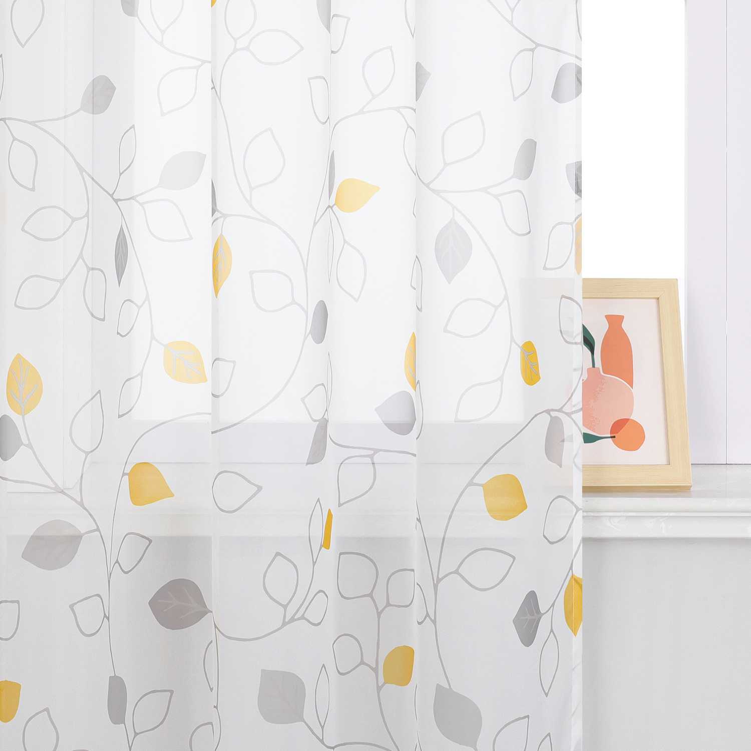 Dieser weiße Voile-Vorhang mit grauen Ranken und gelben sowie grauen Blättern sorgt für eine angenehme Lichtdurchlässigkeit. Neben dem Vorhang hängt ein Bild in einem Holzrahmen. Der Vorhang bringt eine einfache, frische Atmosphäre und eignet sich ideal für Wohnzimmer oder Schlafzimmer, um eine warme und helle Stimmung zu schaffen.