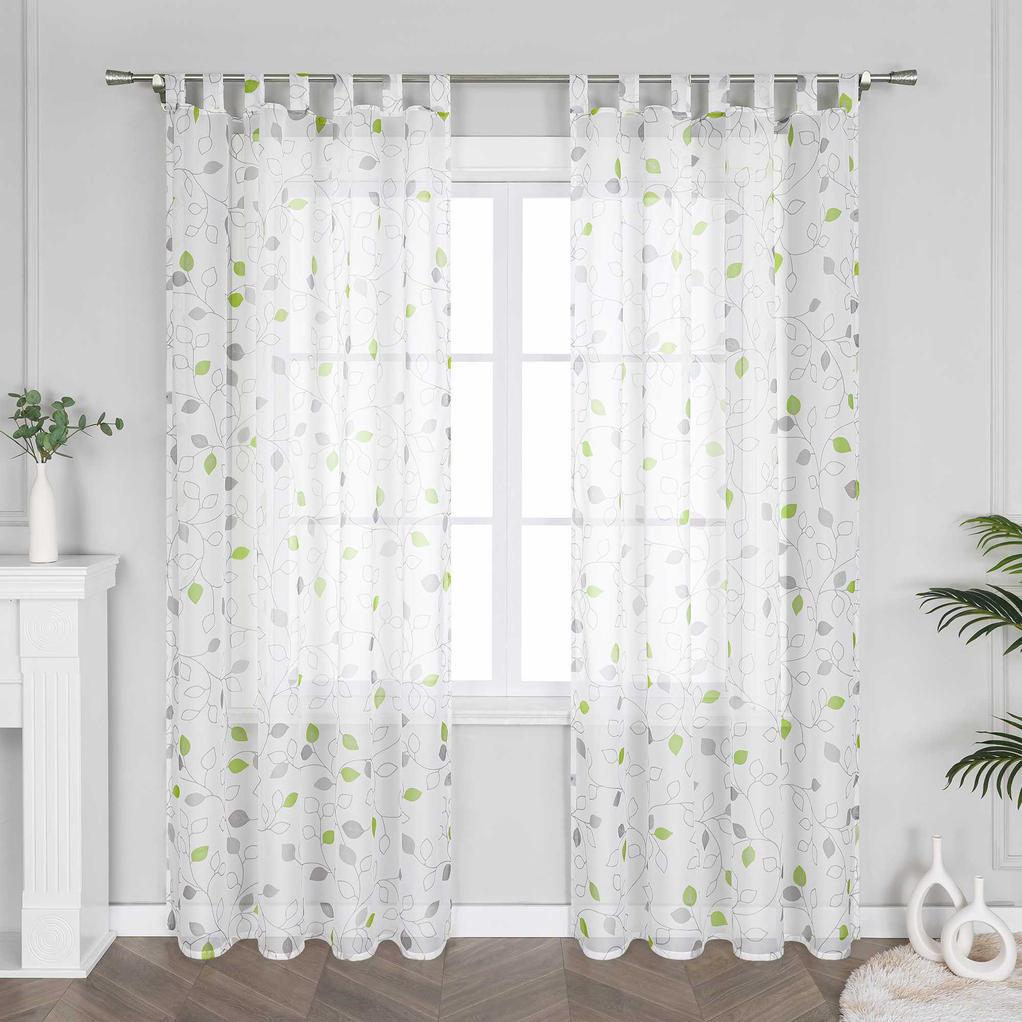 Das Bild zeigt weiße Vorhänge mit grünen und grauen Blättermustern. Diese Vorhänge gehören zur Wohnungseinrichtung und verleihen dem Raum eine natürliche, gemütliche Atmosphäre. Sie passen zu verschiedenen Einrichtungsstilen wie Minimalismus und Landhausstil.