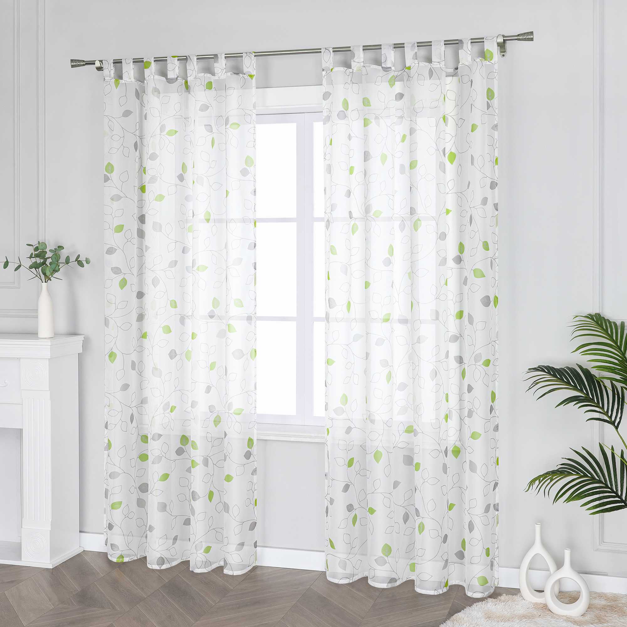 Dies ist ein weißer Voile-Vorhang mit grünen und grauen Blättermustern. Der Vorhang hängt an einer Metallstange vor dem Fenster und wird von grünen Pflanzen und minimalistischen weißen Dekorationsstücken umrahmt. Der Voile bietet eine gute Lichtdurchlässigkeit und sorgt für sanftes Licht im Raum. Das frische Muster verleiht dem Raum eine natürliche Atmosphäre und ist ideal für Schlafzimmer, Wohnzimmer und andere Räume, um die Schönheit und den Komfort des Zuhauses zu steigern.